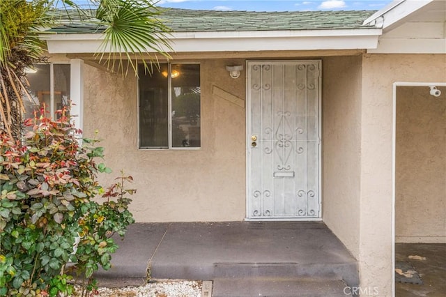 view of exterior entry with stucco siding and roof with shingles