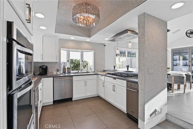 kitchen with stainless steel appliances, a raised ceiling, hanging light fixtures, and white cabinets