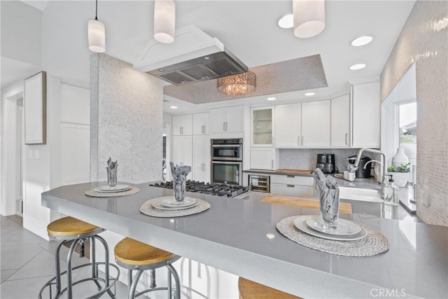 kitchen featuring a kitchen bar, custom exhaust hood, appliances with stainless steel finishes, kitchen peninsula, and white cabinets