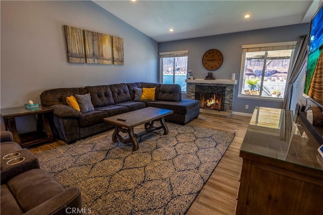 living room with lofted ceiling, a stone fireplace, and light hardwood / wood-style flooring