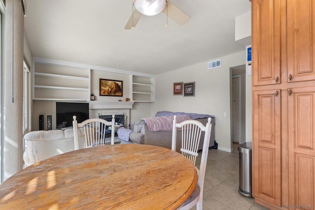 tiled dining room with ceiling fan and a fireplace