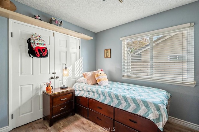 bedroom with a closet, a textured ceiling, and light wood-type flooring