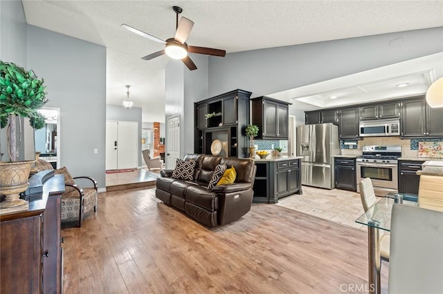 living room with a textured ceiling, high vaulted ceiling, ceiling fan, and light wood-type flooring