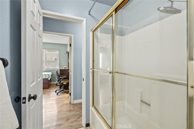 bathroom featuring hardwood / wood-style flooring and bath / shower combo with glass door