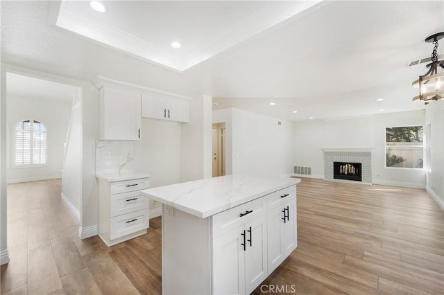 kitchen with light stone counters, a center island, light hardwood / wood-style flooring, and white cabinets