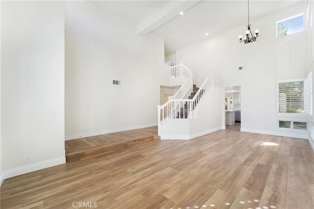 unfurnished living room featuring beamed ceiling, wood-type flooring, a towering ceiling, and a notable chandelier