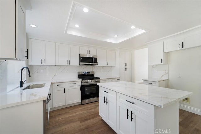 kitchen with a tray ceiling, stainless steel appliances, a center island, and white cabinets