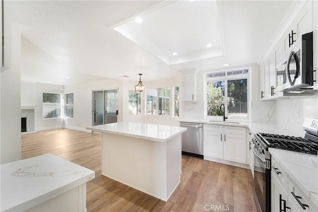 kitchen featuring sink, white cabinetry, stainless steel appliances, a center island, and light stone countertops