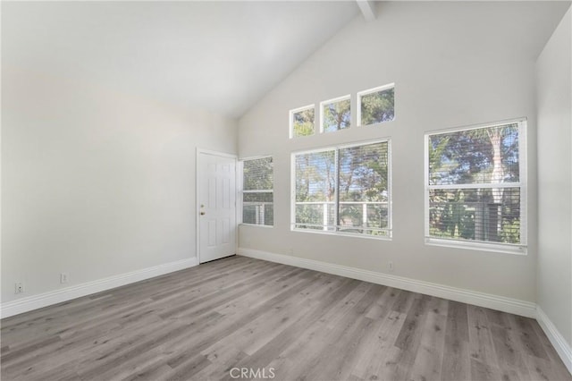 spare room featuring beam ceiling, high vaulted ceiling, and light wood-type flooring