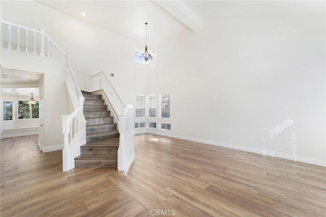 staircase with a high ceiling, hardwood / wood-style flooring, a chandelier, and beam ceiling