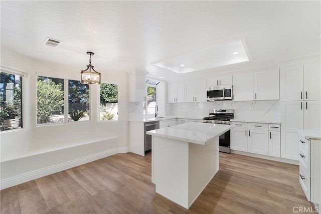 kitchen featuring pendant lighting, stainless steel appliances, white cabinets, a kitchen island, and a raised ceiling