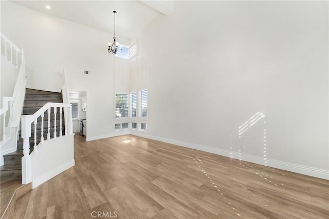 unfurnished living room with an inviting chandelier, light hardwood / wood-style floors, and a high ceiling