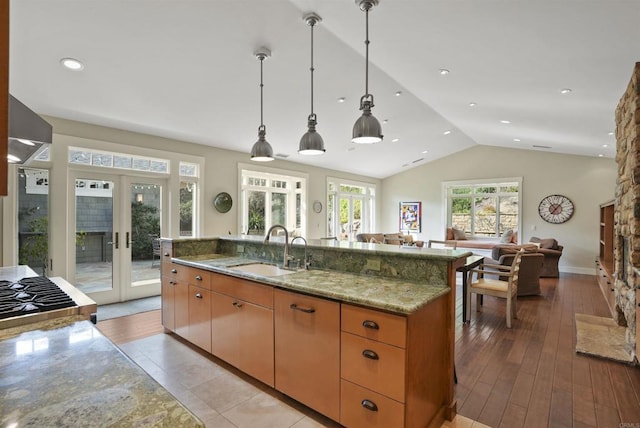 kitchen featuring french doors, lofted ceiling, sink, light stone counters, and hanging light fixtures