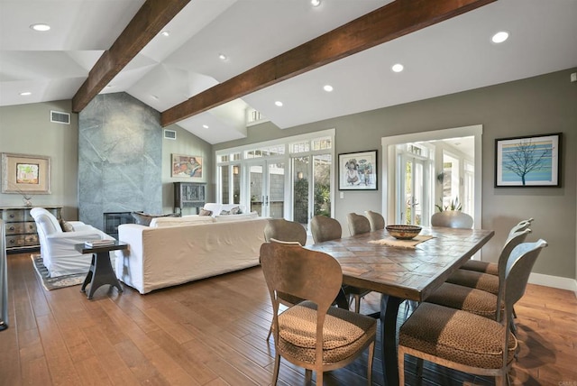 dining area with french doors, wood-type flooring, a tiled fireplace, and lofted ceiling with beams