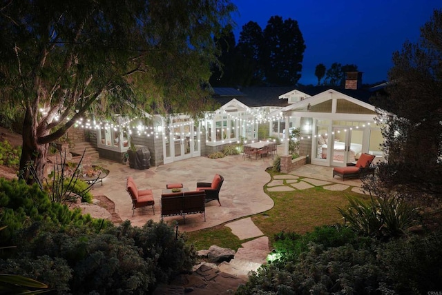 back house at twilight with french doors, an outdoor living space, and a patio area