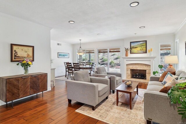 living area featuring baseboards, visible vents, ornamental molding, hardwood / wood-style floors, and a fireplace