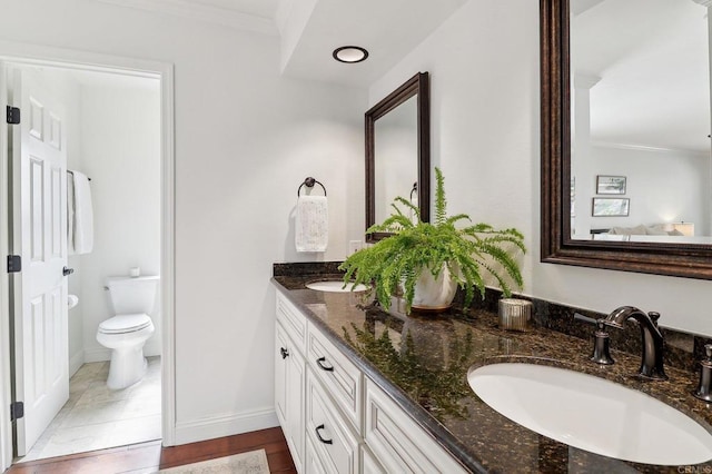 full bathroom featuring double vanity, toilet, ornamental molding, a sink, and baseboards