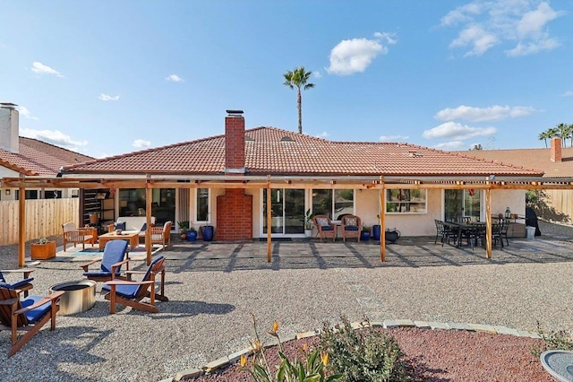 rear view of property with a fire pit, a patio, a tile roof, a chimney, and fence