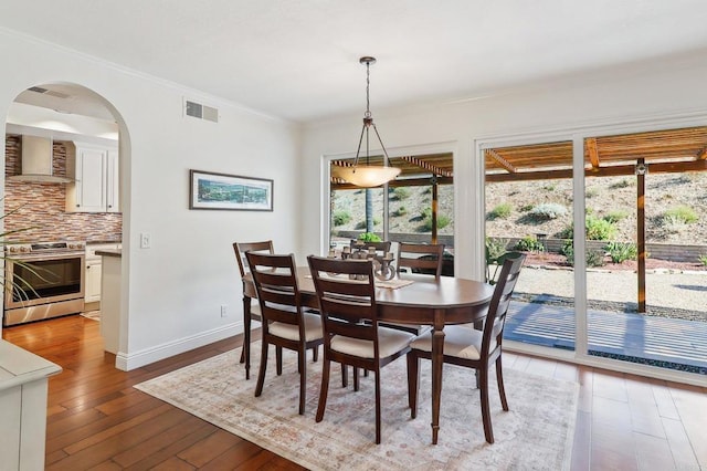 dining room with arched walkways, crown molding, visible vents, baseboards, and hardwood / wood-style flooring