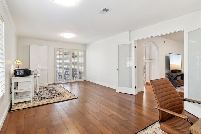 interior space with arched walkways, wood finished floors, visible vents, baseboards, and crown molding