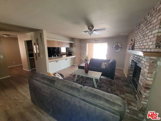 living room featuring hardwood / wood-style flooring, ceiling fan, a fireplace, and sink