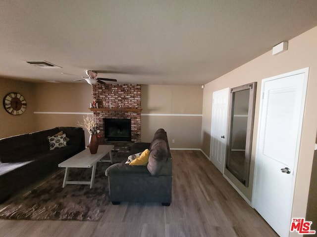 living room with a brick fireplace, wood-type flooring, and ceiling fan