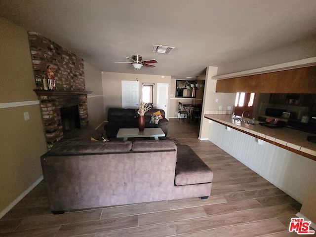 living room with ceiling fan, a fireplace, sink, and light wood-type flooring