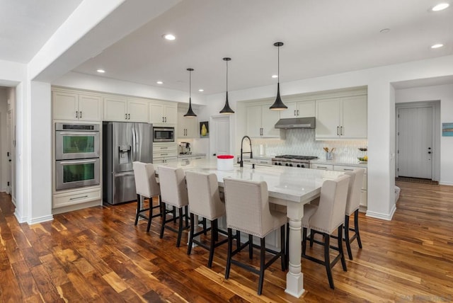 kitchen with appliances with stainless steel finishes, a kitchen breakfast bar, light stone countertops, and a large island with sink