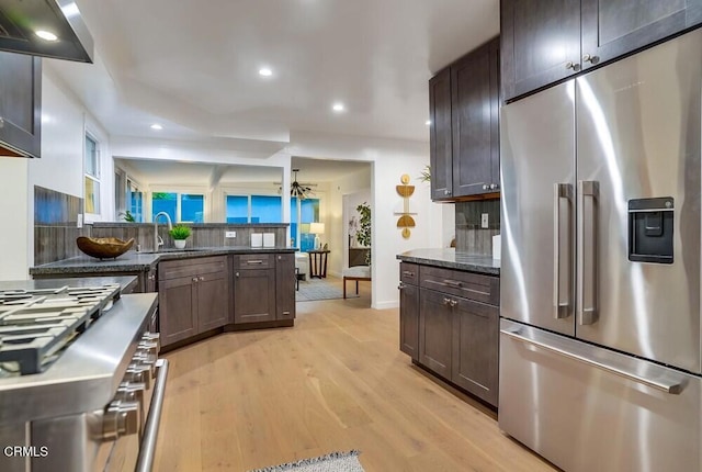 kitchen with dark brown cabinetry, sink, high end appliances, dark stone countertops, and range hood