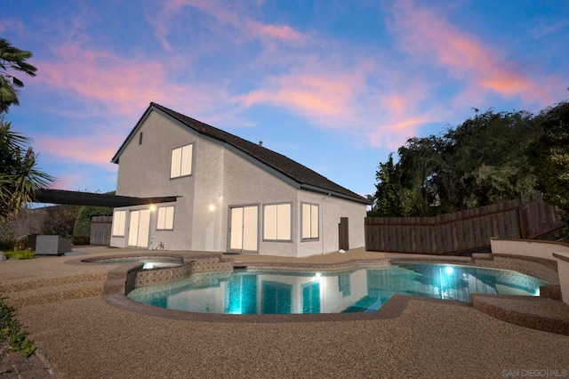 pool at dusk featuring a patio and an in ground hot tub