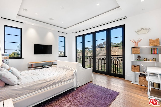 bedroom featuring a raised ceiling, light hardwood / wood-style flooring, and access to outside