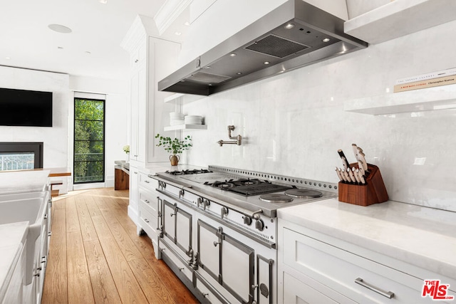 kitchen featuring stainless steel gas cooktop, exhaust hood, light wood-type flooring, a fireplace, and white cabinets