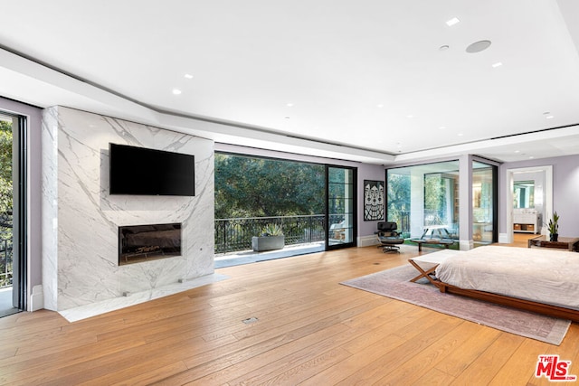 bedroom with access to exterior, a high end fireplace, and light hardwood / wood-style floors