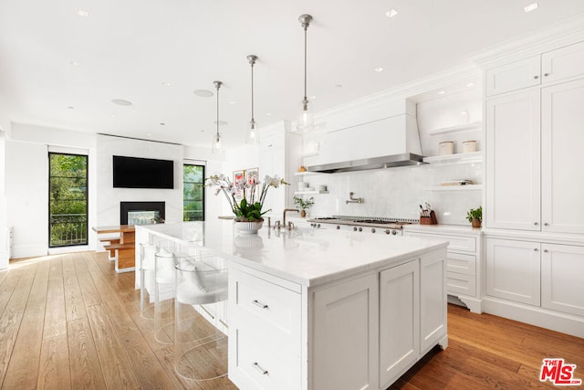 kitchen featuring white cabinetry, light wood-type flooring, a fireplace, and a center island with sink