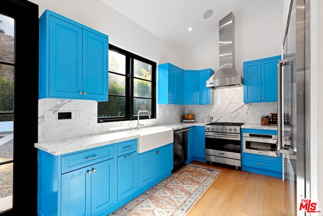 kitchen featuring wall chimney exhaust hood, lofted ceiling, sink, light stone counters, and stainless steel appliances