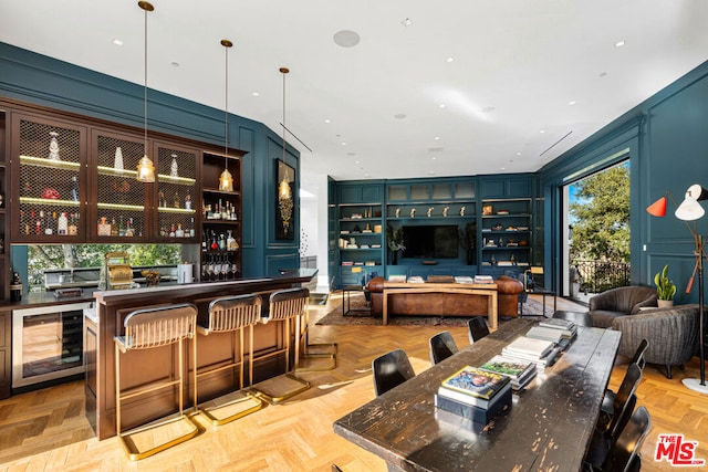 bar with light parquet flooring, decorative light fixtures, blue cabinets, and beverage cooler