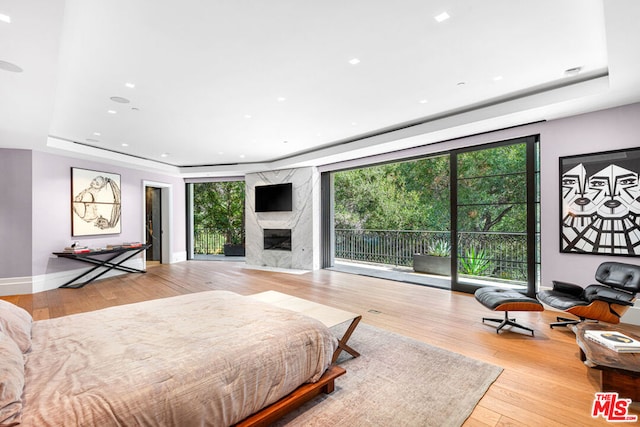 bedroom with multiple windows, light hardwood / wood-style flooring, a premium fireplace, and access to outside