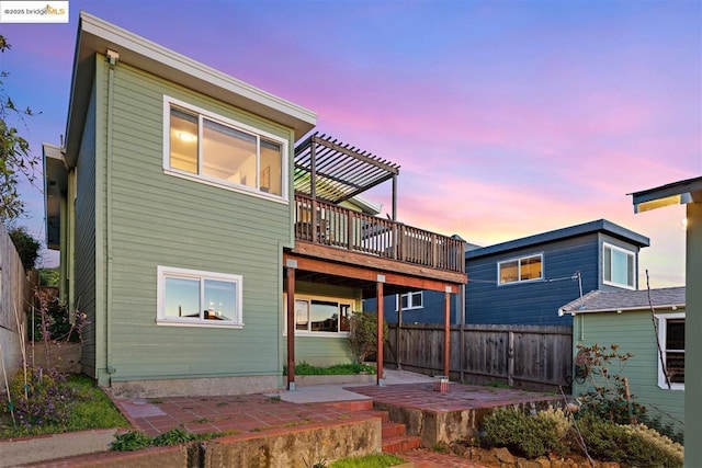 back house at dusk with a patio, a deck, and a pergola