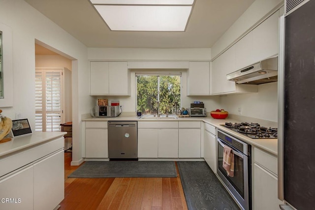 kitchen with stainless steel appliances, wood-type flooring, sink, and white cabinets