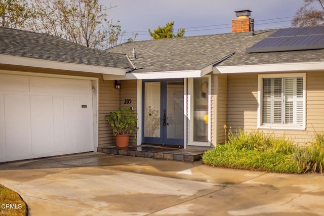 view of exterior entry featuring a garage, french doors, and solar panels