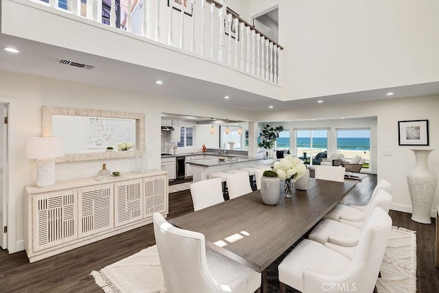 dining area featuring a water view, dark wood-type flooring, and a high ceiling