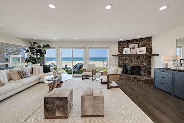 living room with a view of the beach, hardwood / wood-style floors, a stone fireplace, and a water view