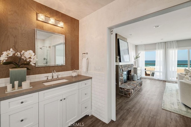 bathroom with a fireplace, hardwood / wood-style flooring, vanity, an enclosed shower, and a water view