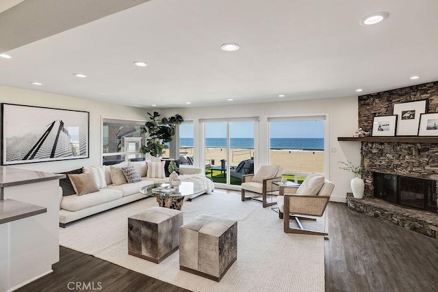 living room featuring hardwood / wood-style floors, a stone fireplace, a beach view, and a water view