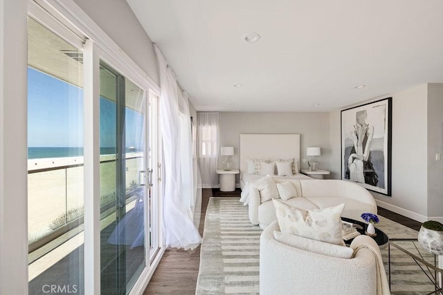 bedroom with a water view, access to exterior, dark wood-type flooring, and a view of the beach