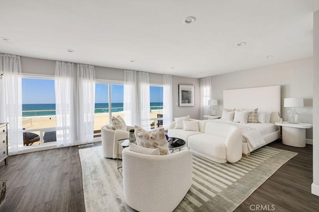 bedroom with hardwood / wood-style flooring, a water view, access to outside, and a beach view