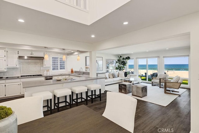 interior space with white cabinetry, a kitchen bar, decorative backsplash, hanging light fixtures, and a water view