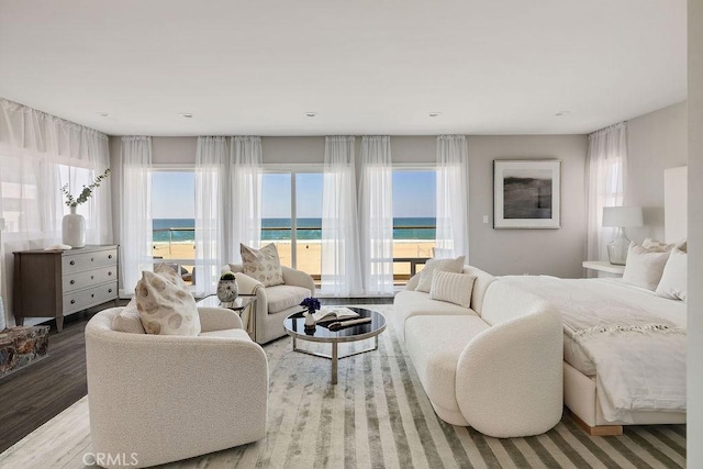 bedroom with multiple windows, wood-type flooring, a water view, and a view of the beach