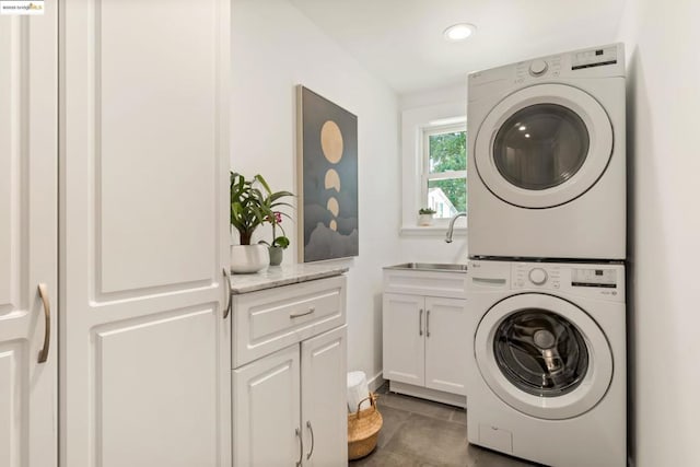 washroom featuring cabinets, stacked washer and dryer, and sink