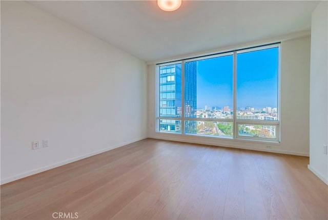 unfurnished room featuring baseboards, light wood-style floors, and a city view